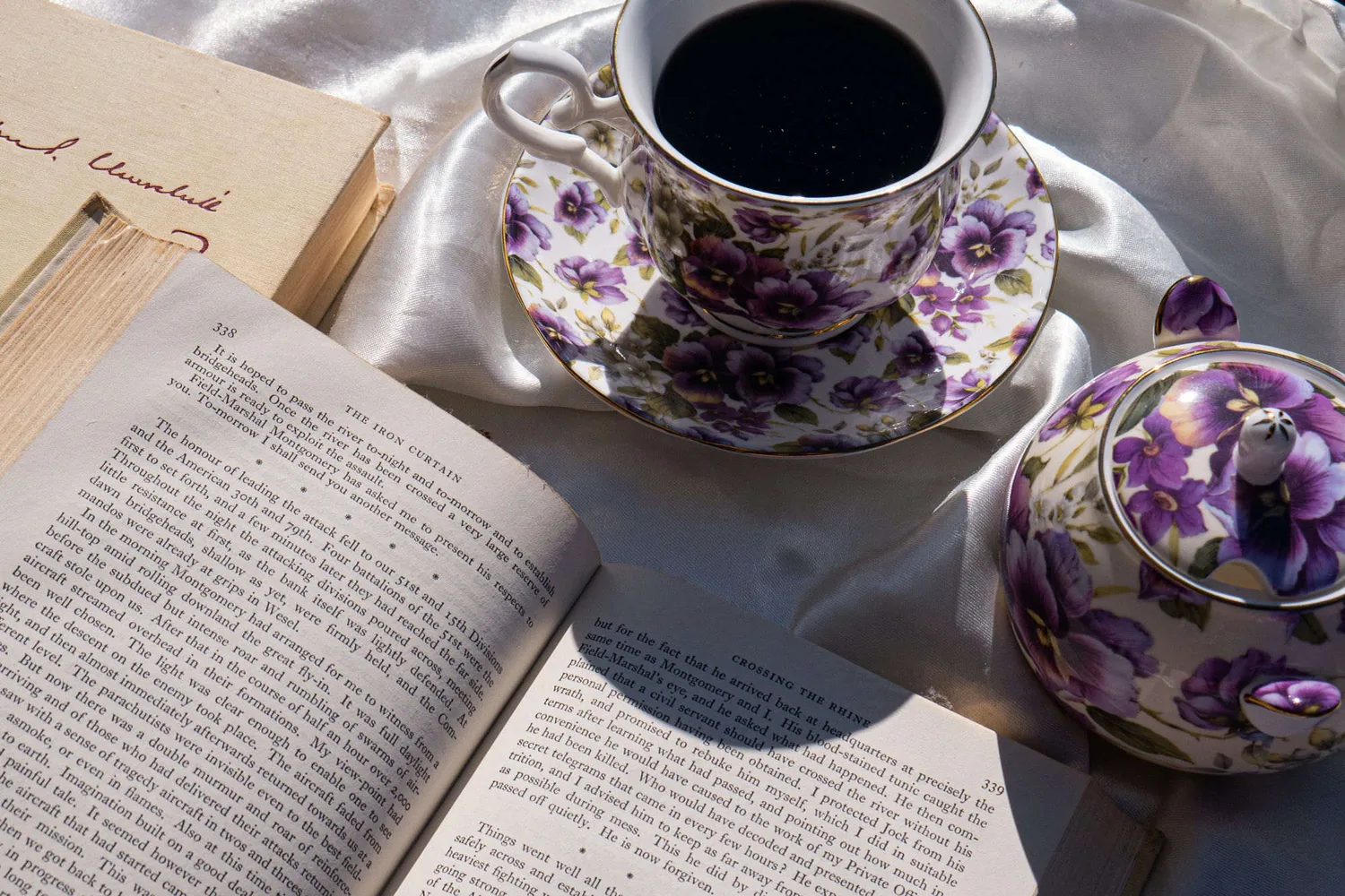 An old book open beside a floral teacup in soft morning light