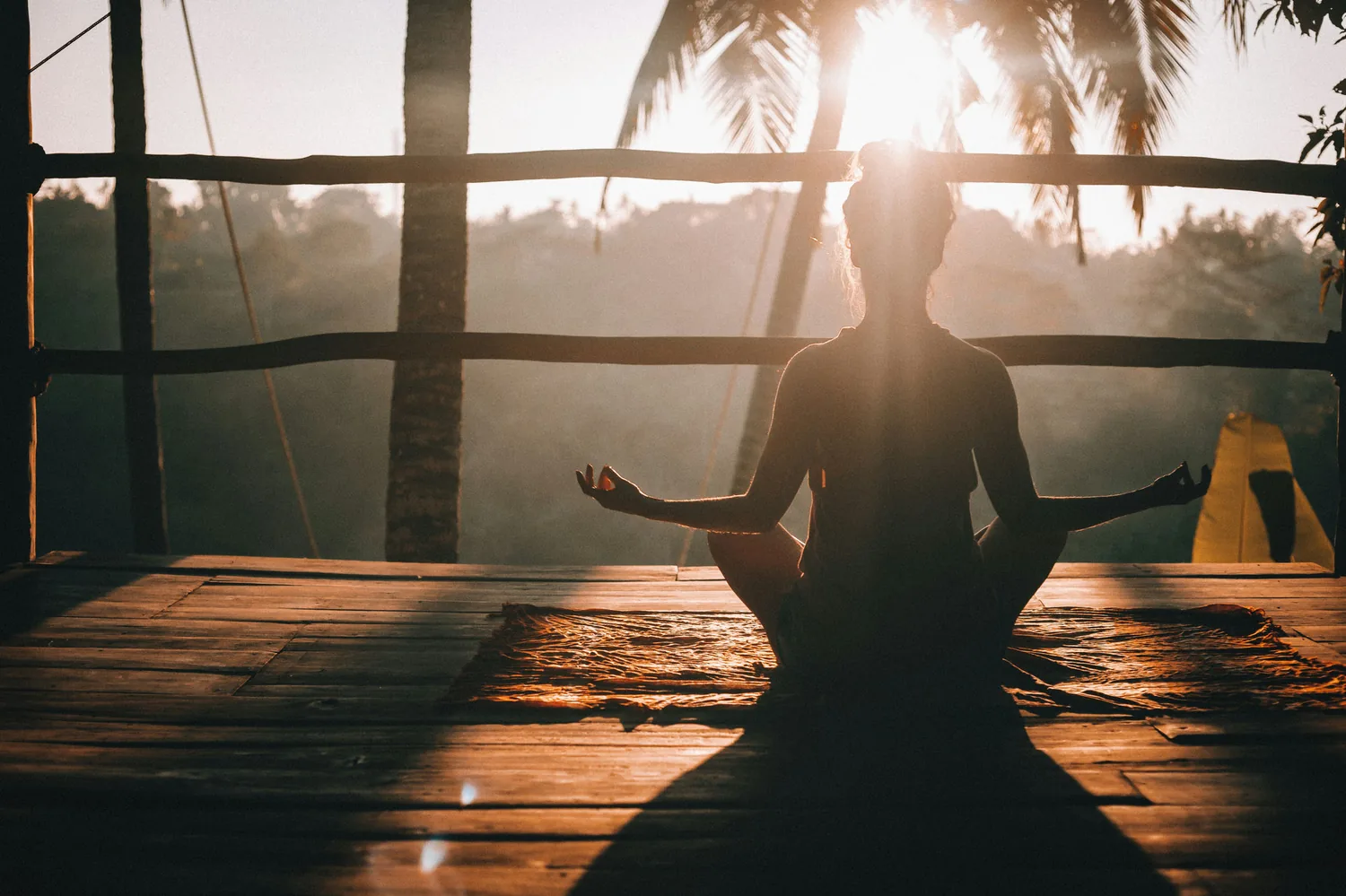 A person meditating in a lotus pose, backlit by a golden sunrise